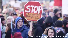 A man in a group of protesters holds up a protest sign, a red stop sign with the words Stop Nazis