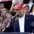 Stariji muškarac s crvenom kapom na glavi na kojoj piše "Učinimo Ameriku ponovo velikom", govori za mikrofonom